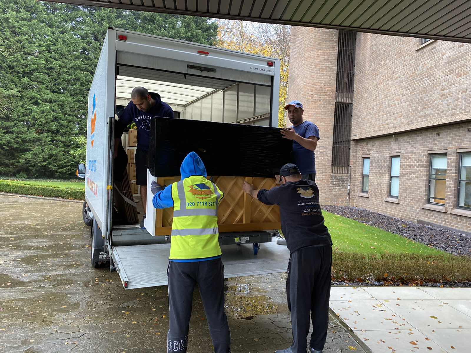 Professional London movers carefully pushing covered piano onto moving truck